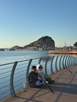 Senior couple fishing on a scenic waterfront pier during a sunny day.