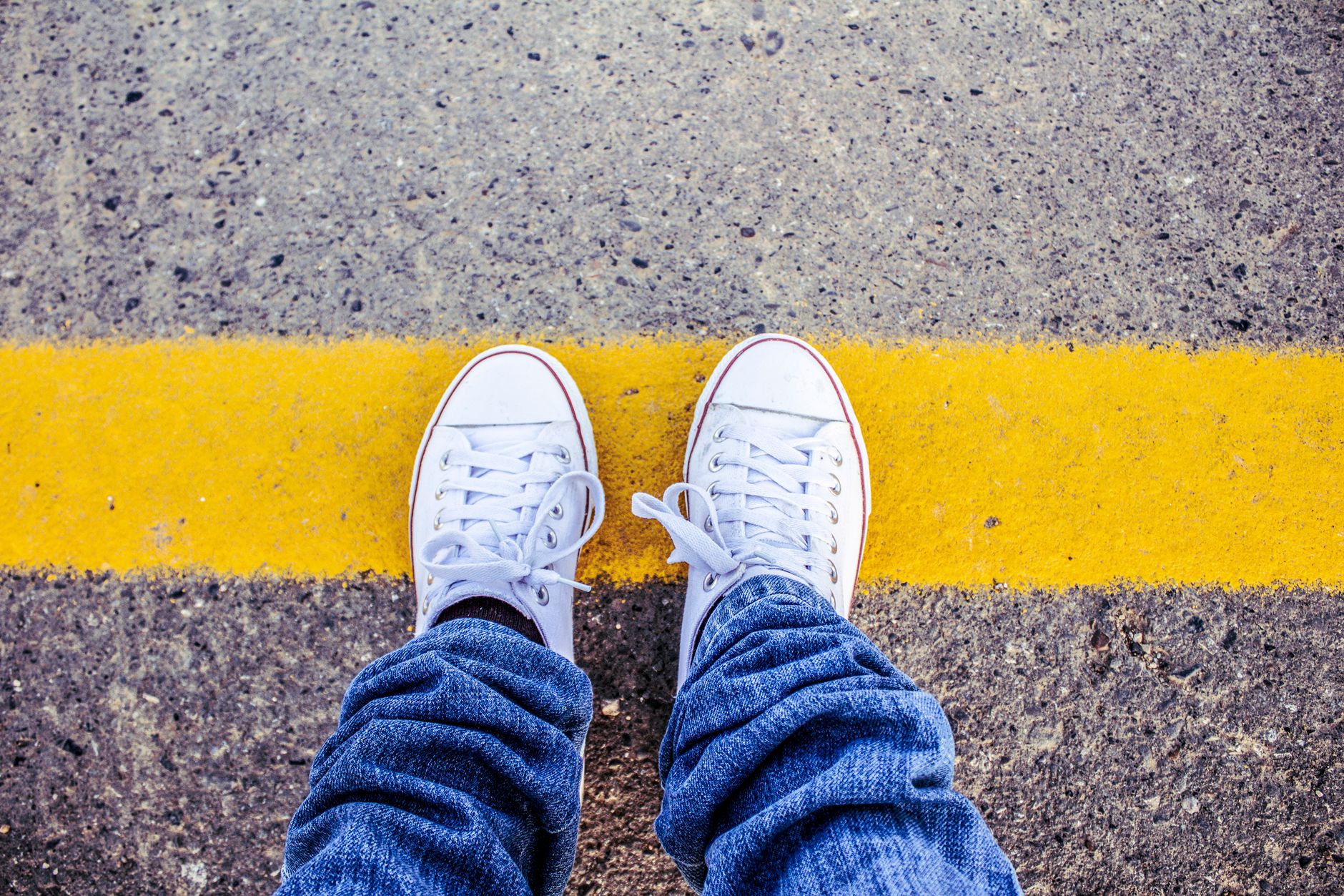 Close-up of white sneakers on pavement with a yellow line, symbolizing boundaries.
