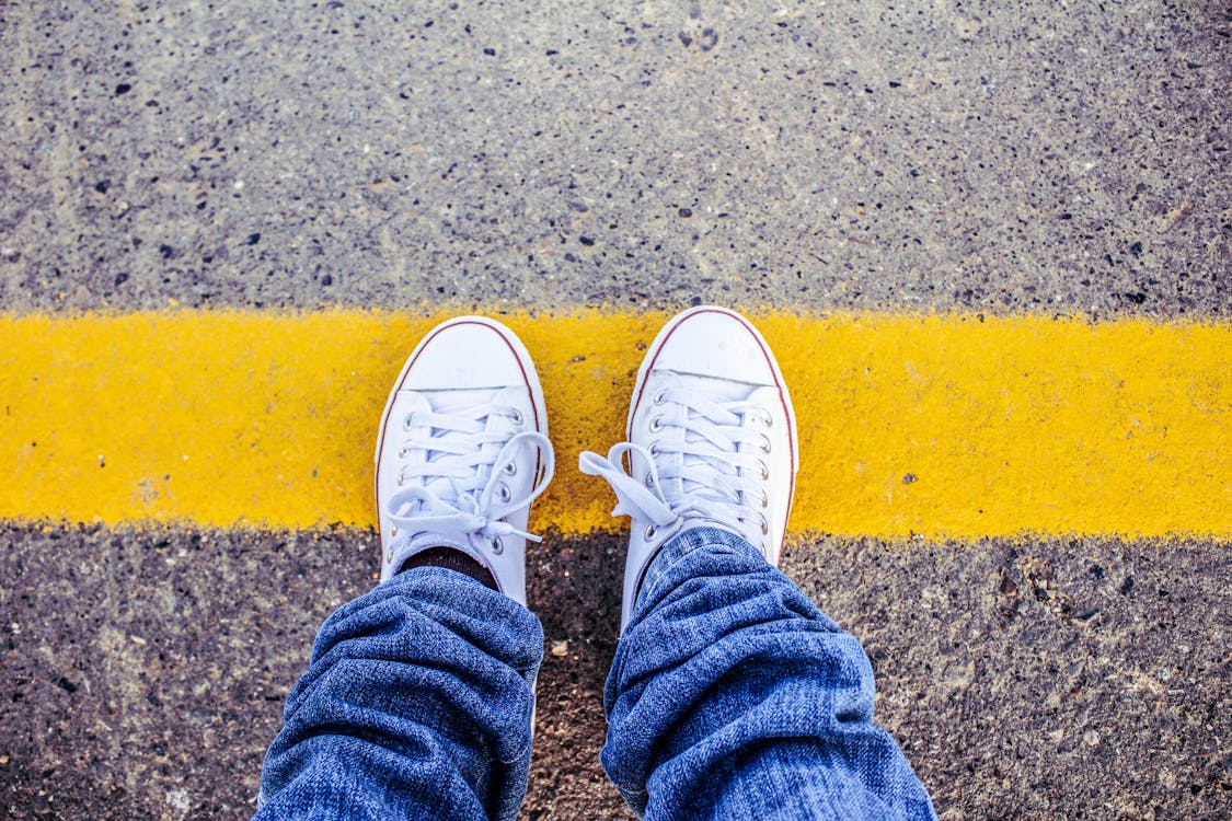 Free Close-up of white sneakers on pavement with a yellow line, symbolizing boundaries. Stock Photo