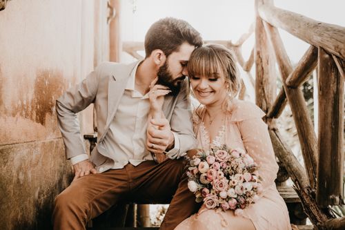 Free A bride and groom sharing a tender moment outdoors with a rustic backdrop. Stock Photo