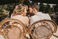 一对年轻夫妇坐在户外的柳条椅上，紧紧依偎，共享浪漫时刻