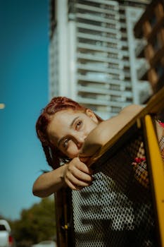 一位年轻女子靠在城市景观的栅栏旁，若有所思地凝视着远方