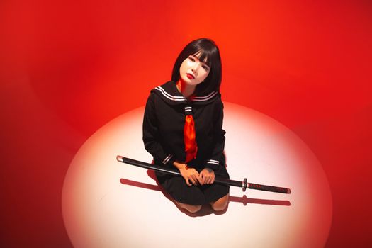 A young woman in a sailor uniform holding a samurai sword in a high-contrast, red-lit setting.