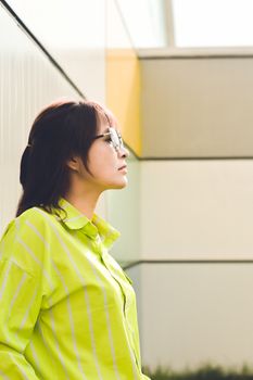 Woman in neon striped shirt posing against a modern architectural wall outdoors.