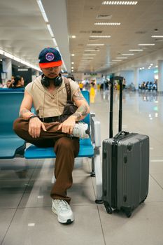 Stylish man in airport lounge with luggage, headphones, millennial fashion, ready for journey.