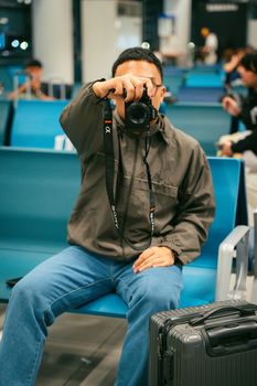 A person capturing a moment with a camera in an airport waiting area, luggage visible nearby.