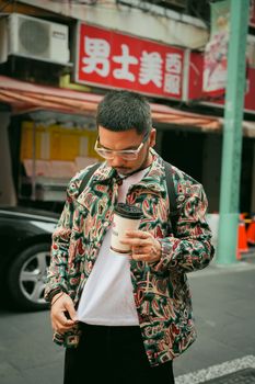 Young man with a trendy jacket and coffee in a culturally vibrant urban street.
