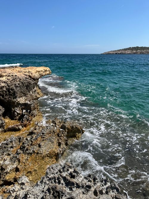 Free A scenic view of the rocky shoreline meeting the vibrant turquoise sea on a sunny day. Stock Photo