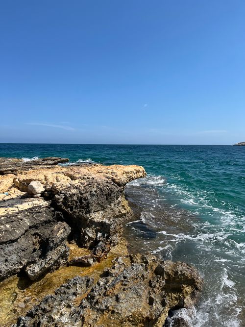 Free Breathtaking view of a rocky coastline with clear blue ocean waves and bright sunny skies. Stock Photo