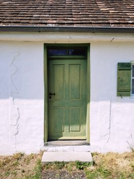 A rustic green door on a weathered white cottage under bright sunlight. Ideal for architecture and travel themes.