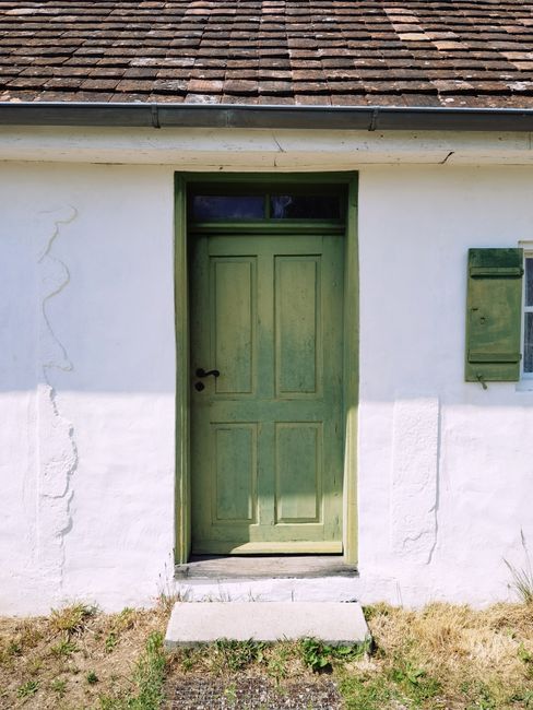 A rustic green door on a weathered white cottage under bright sunlight. Ideal for architecture and travel themes.