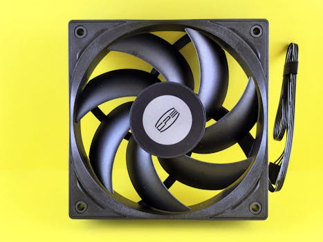 Black computer cooling fan on a vibrant yellow background, highlighting its design.