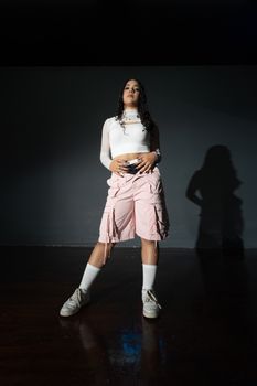 A young Latina dancer posing confidently in a minimalist indoor setting.