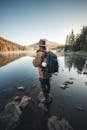 Man in Brown Jacket and Brown Hat Standing on Rock Near Lake