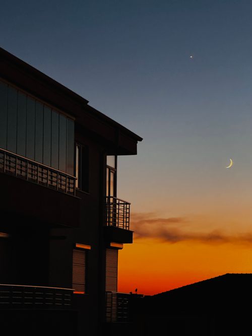 Free A building silhouette against a vivid sunset sky with a crescent moon and star visible. Stock Photo