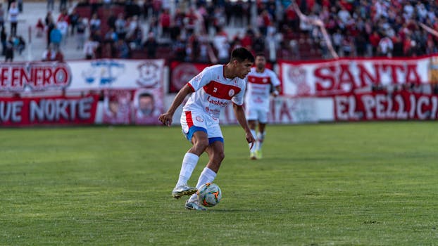 Soccer player wearing red and white uniform dribbling on a field during a match.