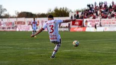 A football player kicks the ball on the field during an outdoor match with spectators.