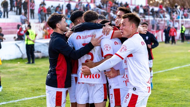 Dynamic image of a soccer team celebrating a goal during an outdoor match, highlighting teamwork and excitement.