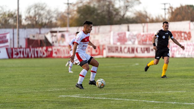Dynamic shot of a soccer player in red and white kit dribbling on the pitch during a match.