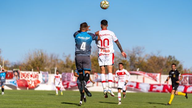 Soccer players in uniforms jumping to head the ball during an outdoor match on a sunny day.