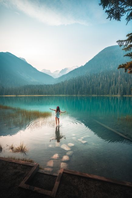 A woman stands peacefully in a clear Canadian mountain lake surrounded by lush greenery.