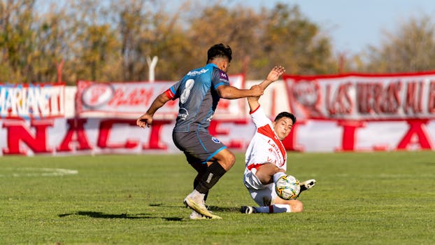 Two players engage in a dynamic soccer tackle on an outdoor field.