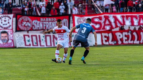 Free Dynamic football scene capturing two players in action during a competitive match with vibrant fan banners in the background. Stock Photo