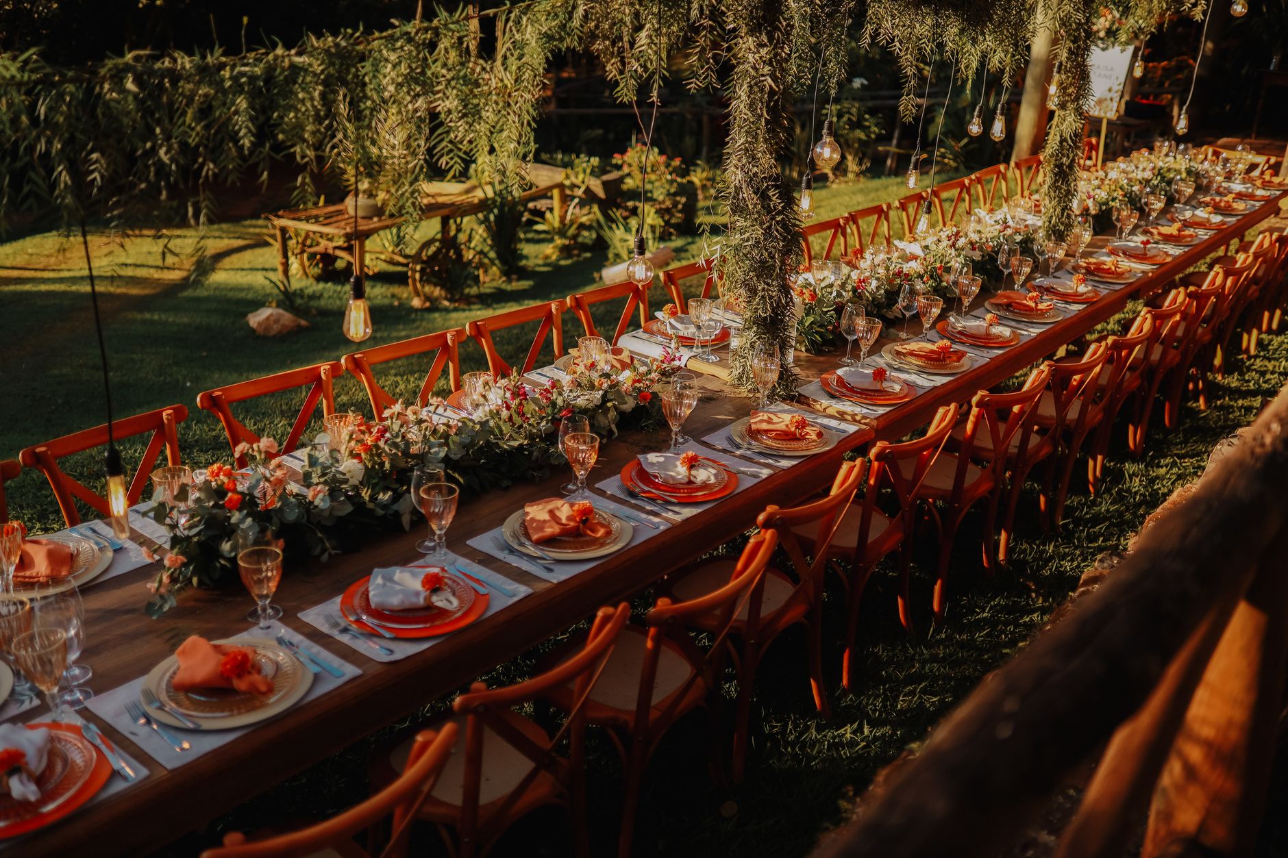 Long outdoor dining table elegantly set in garden setting, perfect for weddings or parties.