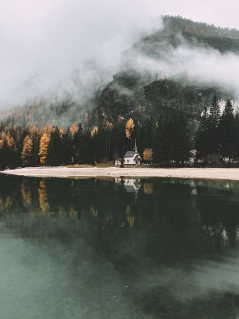 Peaceful autumn landscape of Lake Braies with misty mountains and serene reflections.