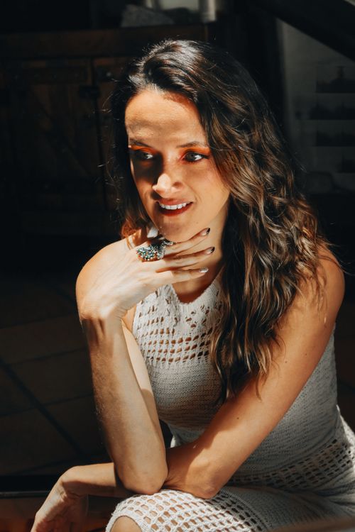 Free A woman in a white lace dress sits in a sunlit room, radiating elegance and warmth. Stock Photo