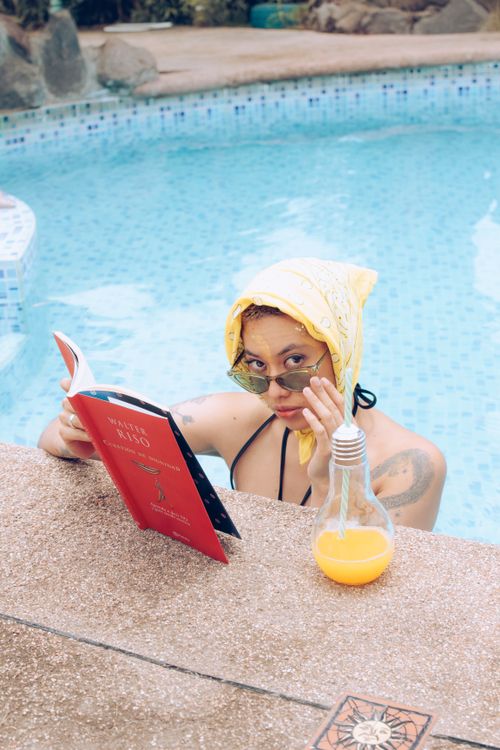 Free A woman enjoying a sunny day by the pool reading a book, creating a perfect summer vibe. Stock Photo