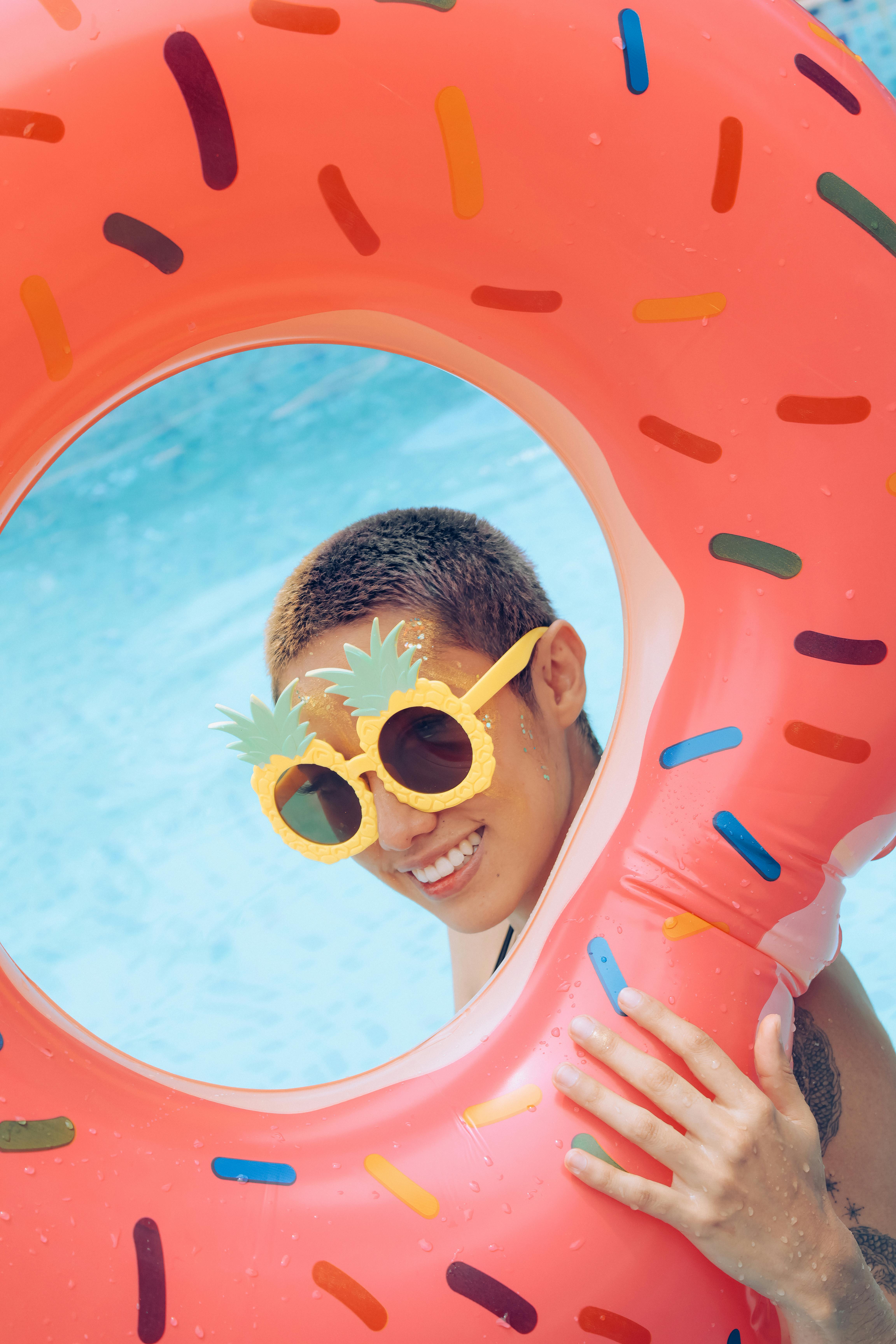 A young person enjoys a sunny pool day with a fun donut-shaped float and playful pineapple sunglasses.