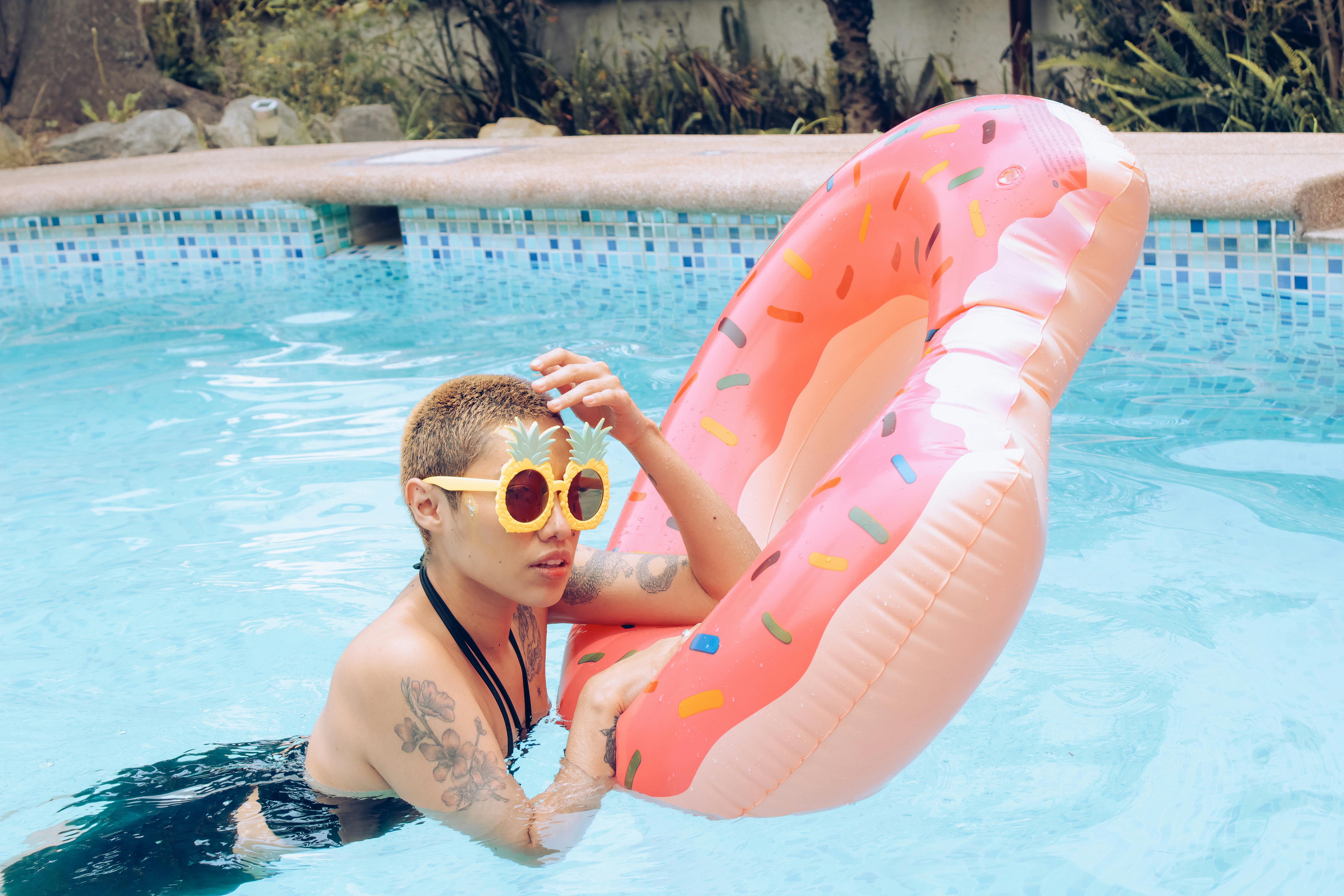 A vibrant summer scene featuring a woman enjoying a pool with tropical sunglasses and a donut float.