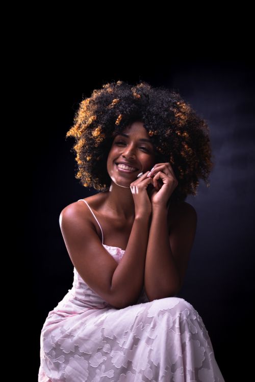 Free Portrait of a joyful woman with curly hair wearing a lace dress, exuding elegance and happiness. Stock Photo