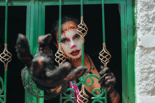 Free A person in clown makeup and costume extends a hand dramatically through a window bar in Quito, Ecuador. Stock Photo