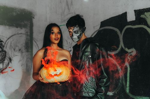 Free Halloween-themed portrait with vibrant costumes and fiery jack-o'-lantern, set in a graffiti-decorated space. Stock Photo