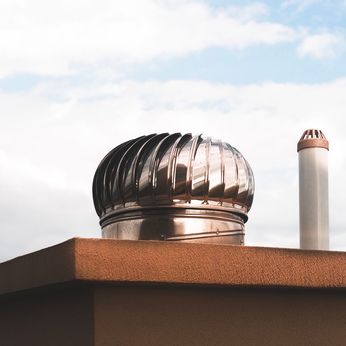 Close-up of a metal rotating roof vent on a sunny day with blue sky in the background.