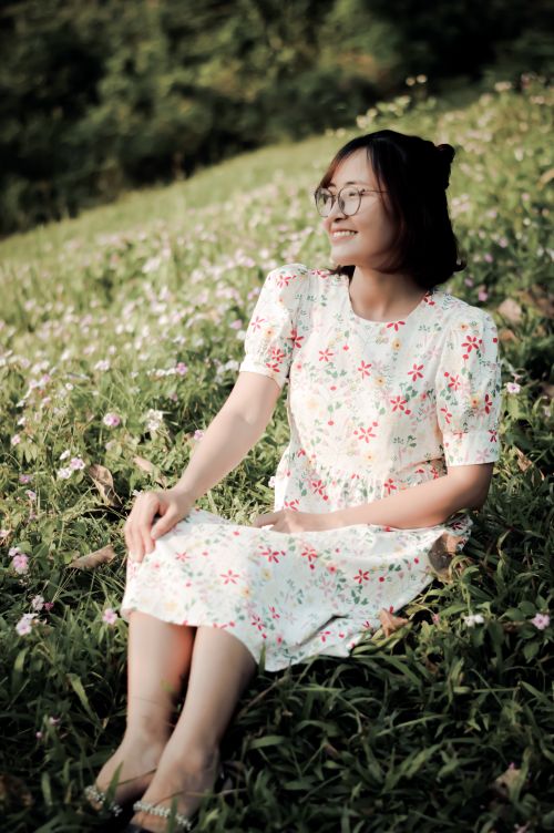 Free Smiling woman sits on a grassy field with wildflowers, embodying joy and tranquility. Stock Photo
