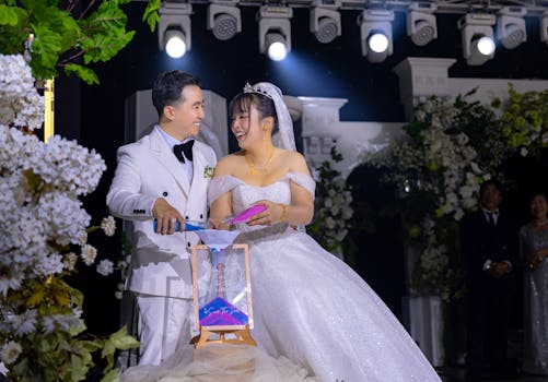 A joyful bride and groom laughing during their wedding ceremony with decorative lighting and floral arrangements.