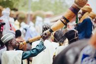 Vibrant scene of a traditional Nigerian festival with a musician playing a large horn amidst colorful attires.