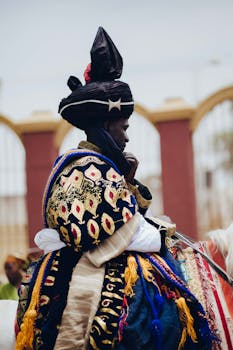 A Nigerian man in elaborate traditional royal attire rides a horse at a cultural festival.
