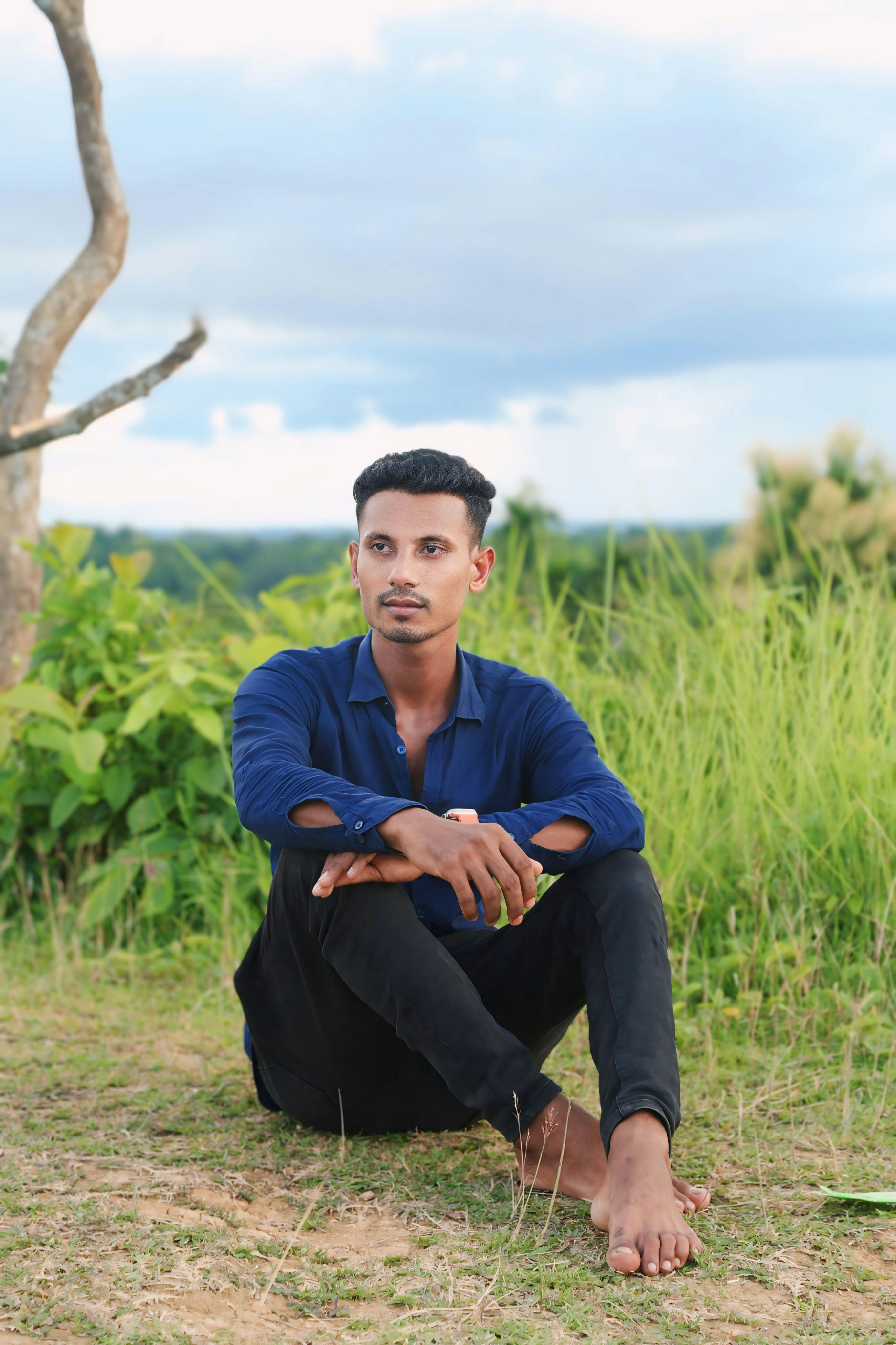 Young man in blue shirt sitting outdoors in a peaceful natural setting.