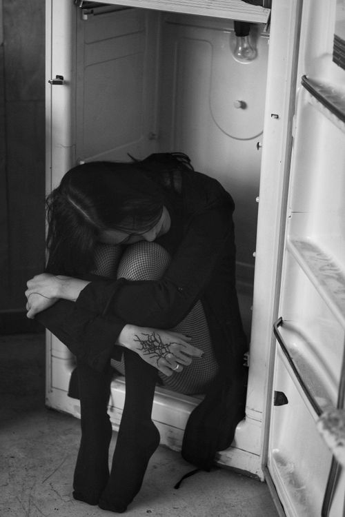 Free Somber black and white image of a woman sitting inside an open fridge, evoking feelings of isolation. Stock Photo
