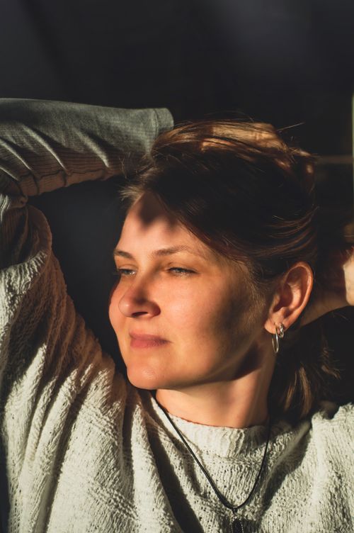 Free Portrait of a relaxed woman basking in warm sunlight inside a room. Stock Photo