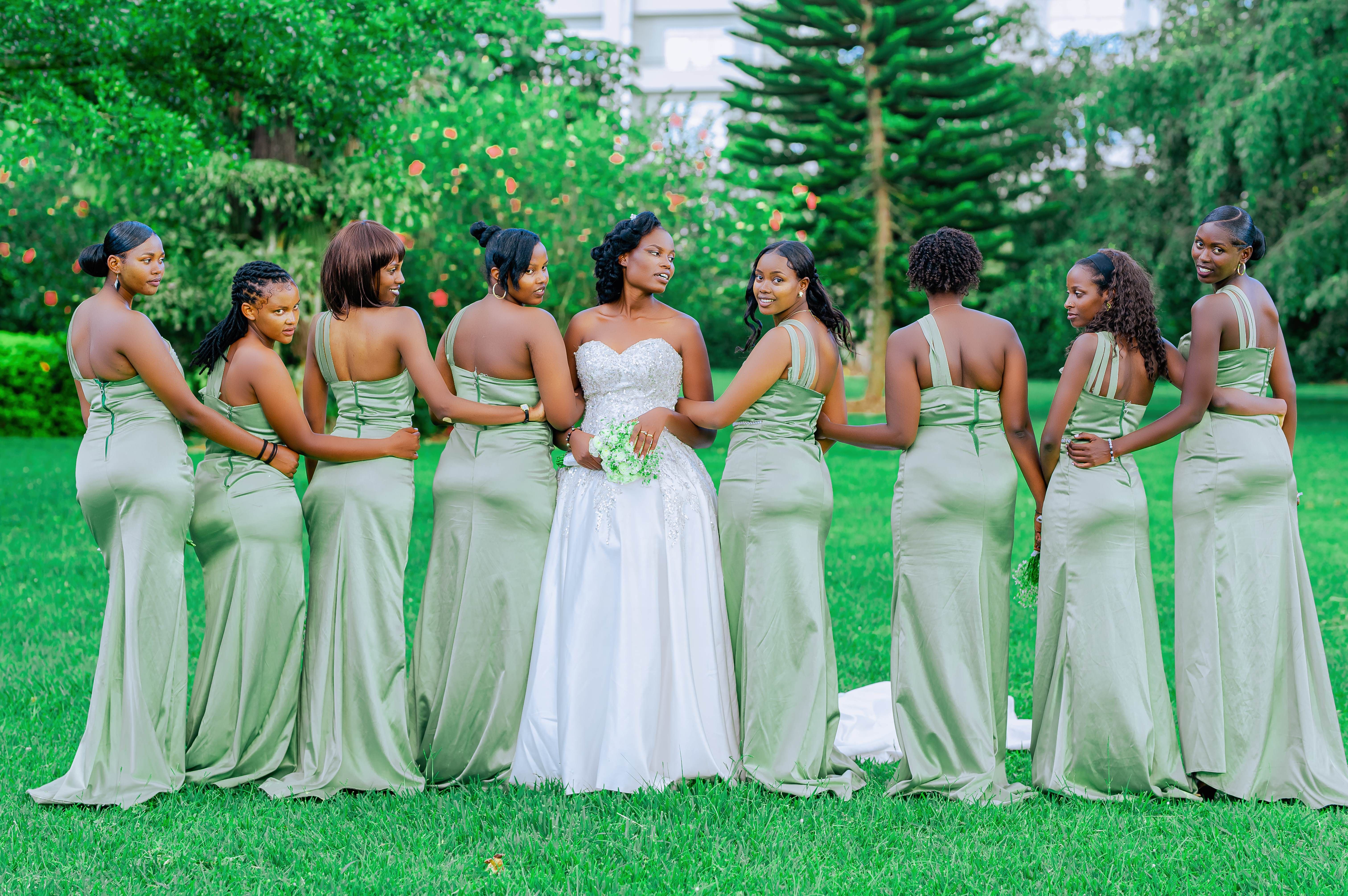 Bride and eight bridesmaids in elegant gowns posing outdoors, showcasing a classic wedding scene.