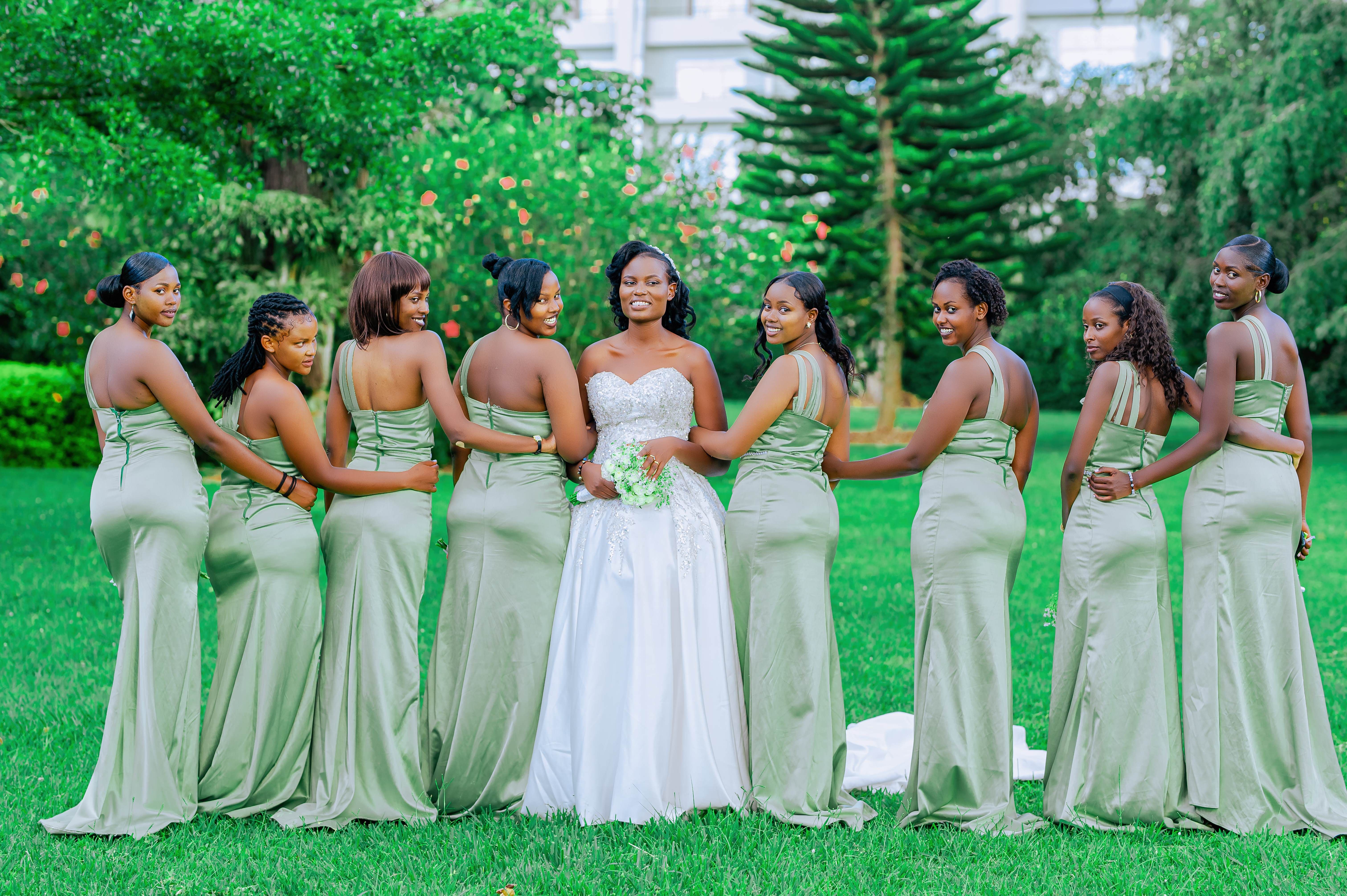 Bride and bridesmaids pose elegantly outdoors in a green garden setting.