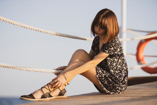 阳光明媚的日子里，一位身穿花卉连衣裙的年轻女子若有所思地坐在海边码头旁