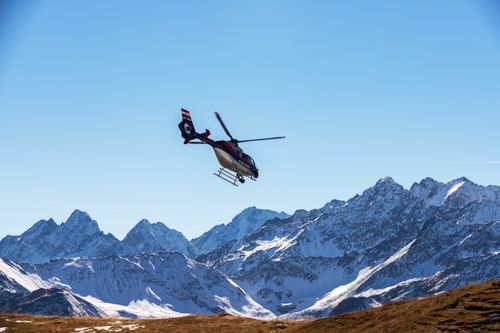 Free A police helicopter flies above snow-covered alpine mountains under a clear blue sky in Korutany, Austria. Stock Photo