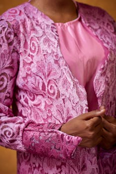 Close-up of a person wearing an elegant pink lace jacket, showcasing intricate floral patterns.