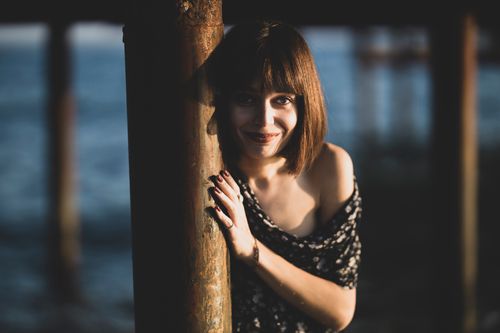 Free A woman leaning against a post, smiling warmly in an outdoor setting. Stock Photo